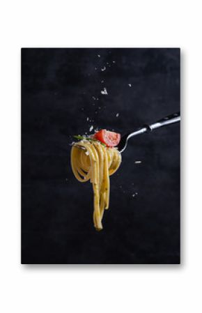 tagliatelle with tomato and pesto on fork. Italian food. Dark background