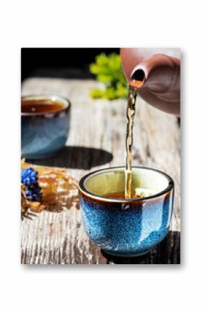 Hot green tea is poured from the teapot into the blue bowl, vintage wooden table, steam rises above the cup. Tea leaves next to the cup. Close-up, tea ceremony, minimalism