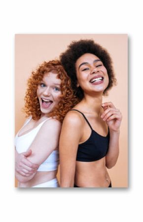 Beauty image of two young smiling and happy women with different body posing in studio for a body positive photoshooting. Mixed female models in lingerie on colored backgrounds. 