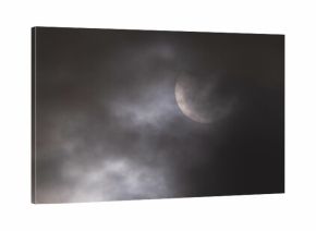 Zaćmienie słońca. Zachmurzone niebo, zza cienkiej warstwy chmur widać słońce w trakcie częściowego zaćmienia. Górna część słońca zasłonięta jest przez księżyc. Na słońcu widoczne są plamy.