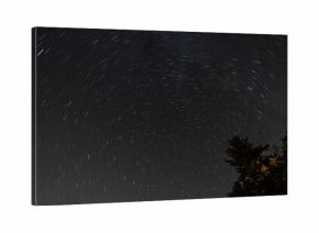 Nocne niebo z dynamicznie zarysowanymi łukami gwiazd oraz rozświetlonymi chmurami, które rozpraszają światło. 