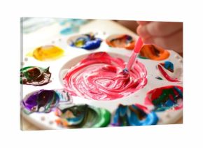 Child mixing paint on a palette of colorful paint