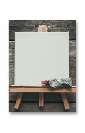 Canvas on easel, paint tube and paintbrush. Old wooden background. Top view. Flat lay. Copy space for text.