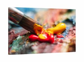 Painter mixes yellow and red oil paint on the palette. Closeup of paint mixing process in art workplace.