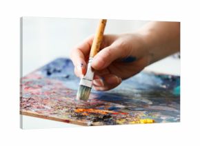 Artist paints a picture of oil paint brush in hand with palette