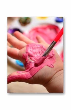 Child painting her hand with pink paint and background with palette of colorful paint