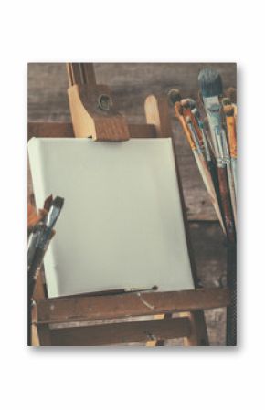 Artistic equipment: empty artist canvas on easel and paint brushes in a artist studio. Retro toned photo.