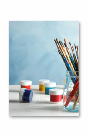 Glass jar with brushes and paints on table against color background. Space for text