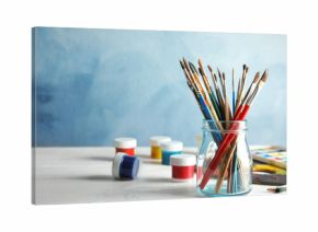 Glass jar with brushes and paints on table against color background. Space for text