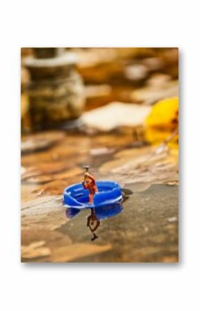 Miniature figurine of a man struggling to row on a bottle cap as a boat on a river