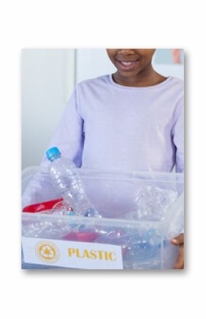 Holding plastic recycling bin, student smiling in classroom at school