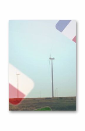 Towering white wind turbine rotating across rural wind farm at sunset, with floating flag icons
