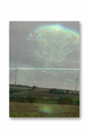 Hovering digital globe overlaying streaming code lines over harvested farmland, with wind turbines