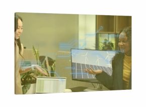 Presenting pair in blazers explaining renewable energy on office monitor, with laptop coffee plants
