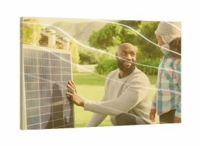 Holding solar panel, kneeling father talking to daughter in front yard, with knit hat and sweater