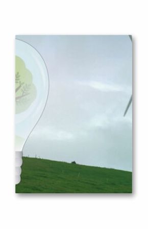 Image of tree in light bulb over wind turbine in green landscape