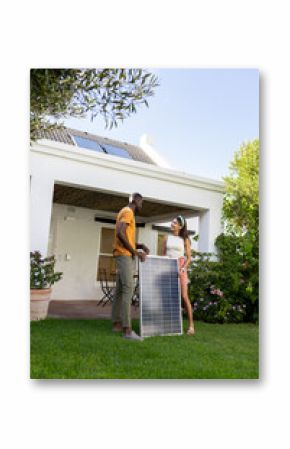 Diverse couple installing solar panel in garden, enjoying sustainable living on vacation, copy space