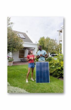 Diverse couple discussing solar panel installation in garden, enjoying sustainable living