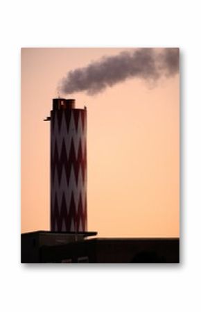 Vertical shot of a red and white chimney with smoke coming out and a pink sky in the background.