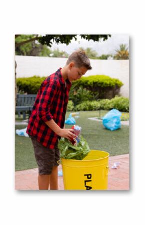 Plastic bottles and green reusable bag being placed into yellow recycling bin on patio
