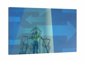 Standing technician wearing safety vest holding handrails on stairs at wind farm, with blue arrows