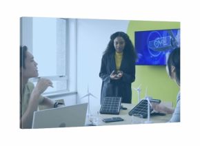 Presenting engineer in black blazer leading discussion at meeting table with wind and solar models