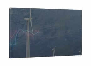 Towering white 3-blade wind turbine centered on slope, showing rocky mountain and blue-pink graph