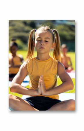 Composite of caucasian schoolgirl meditating in prayer pose while sitting on mat in park