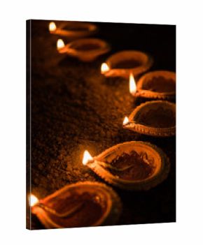 Happy Diwali - many Terracotta diya or oil lamps arranged over clay surface or ground in one line or curved or zigzag form, selective focus    