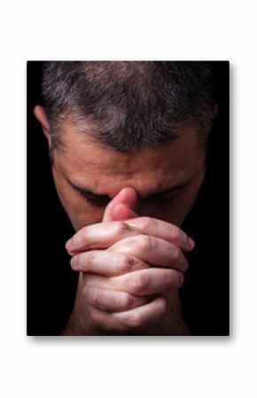 Close up of faithful mature man praying, hands folded in worship to god with head down and eyes closed in religious fervor. Black background. Concept for religion, faith, prayer and spirituality.