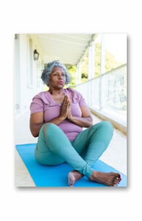 African american senior woman meditating in prayer pose while sitting on mat in balcony, copy space