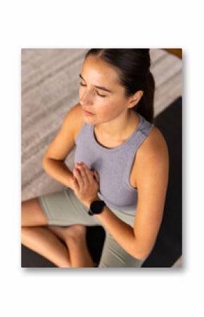 Young Caucasian woman meditating with hands in prayer position on yoga mat