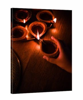 Happy diwali - Hand holding or lighting or arranging diwali diya or clay lamp in brass plate, selective focus