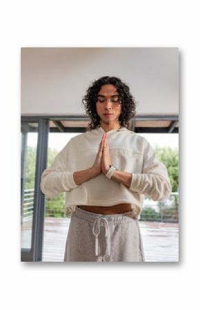 Non-binary person meditating on floor at home wearing cropped hoodie, sweatpants and smartwatch