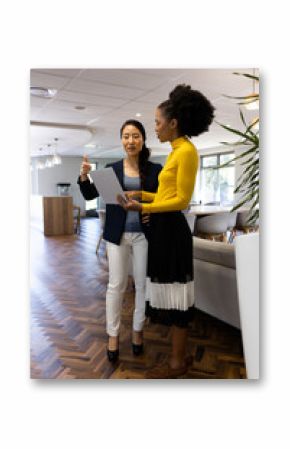 Vertical image of diverse businesswomen with laptop working and talking in office
