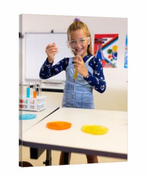 Portrait of happy caucasian schoolgirl with safety goggles doing experiment in lab