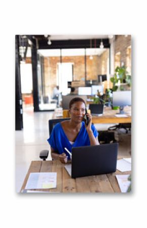 Happy african american casual businesswoman talking on smartphone and having lunch in office
