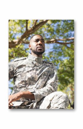 African American soldier in military uniform sits under a tree, looking thoughtful