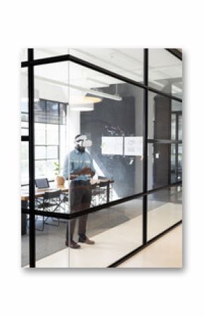 Businessman using VR headset in modern office, standing near glass wall, copy space