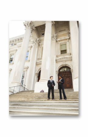 A well dressed man and woman converse on the steps of a legal or municipal building. Could be business or legal professionals or lawyer and client.