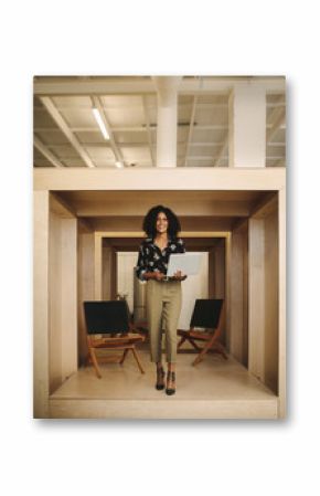 Smiling woman entrepreneur standing in office holding laptop
