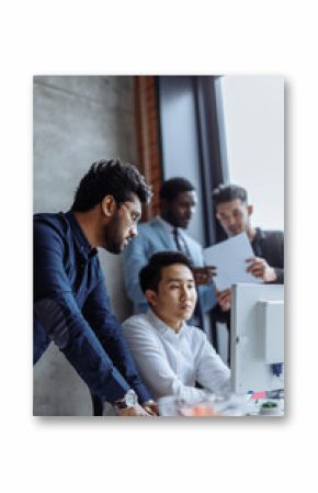 Mixed race group of colleagues talking in friendly manner standing around asian man working on computer, business people enjoy mutual communication.