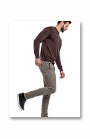 A serious looking man in casual clothes walks in a side view with one leg bent up behind him.