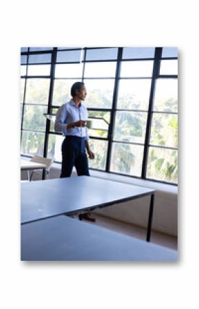Businessman standing by large windows, holding glasses, contemplating outside view