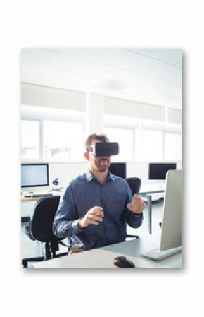 Office worker is wearing VR headset and gesturing at computer desk in open-plan office near windows