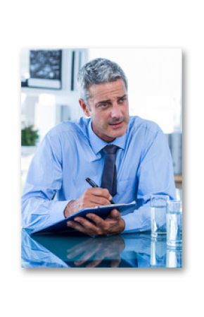 Businessman taking notes on clipboard at office meeting, focusing on discussion