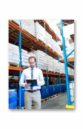 Businessman in warehouse checking inventory on clipboard, surrounded by shelves, copy space
