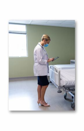 In hospital, doctor wearing mask reviewing patient information on digital tablet