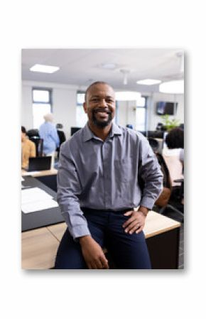 Vertical image of happy african american businessman looking at camera in office