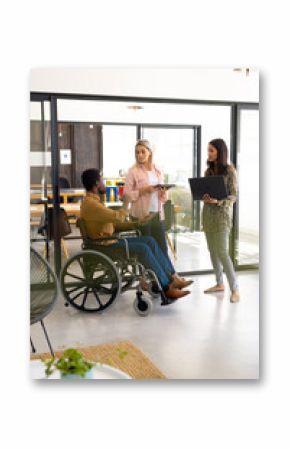 Diverse casual disabled businessman in wheelchair discussing work with colleagues in office